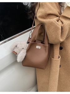 Detail of dark brown lychee leather bucket bag with silver lock and plush rabbit charm