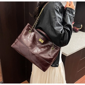 Detail of burgundy quilted tote bag with golden chain strap and metallic twist-lock