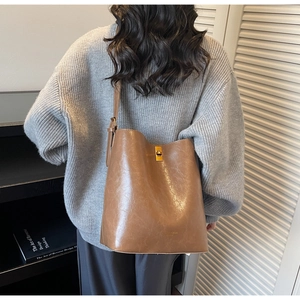 Close-up of a vintage brown leather bucket bag with a golden turn-lock on a model