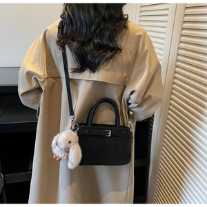 Detail of black suede bucket bag featuring a cute plush bunny charm and crossbody strap