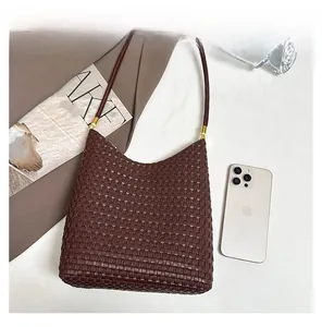 Detail display of brown woven tote bag next to a smartphone for size reference