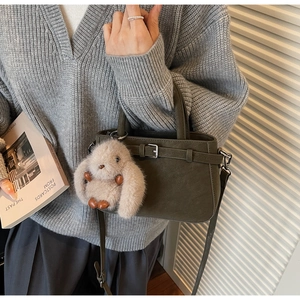 Detail of dark green matte bucket bag with a beige faux fur rabbit charm and metal buckle