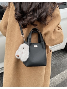Detail of black litchi texture bucket bag with animal charm on a camel wool coat