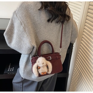 Close-up of burgundy leather bucket bag with cute plush bunny charm on a wool sweater