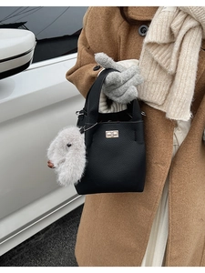 Close-up of black lychee grain bucket bag with gold lock and a white plush rabbit charm