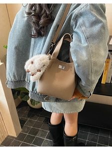 Close-up of khaki lychee grain bucket bag featuring a silver twist lock and plush charm