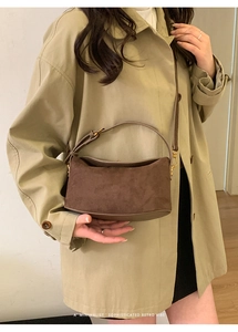 Détail d'un sac demi-lune en daim marron avec boucles dorées porté sur un trench