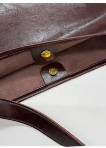Detailed close-up of premium gold magnetic clasps and stitching on a dark brown bucket bag