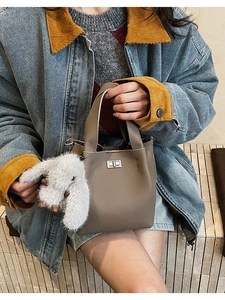 Close-up of beige lychee leather bucket bag with silver twist lock and fluffy bunny charm