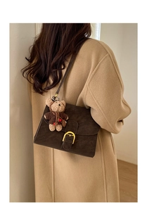 Detail of dark brown matte leather crossbody bag with teddy bear charm on camel coat