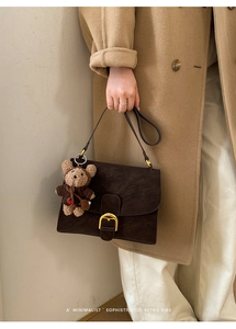 Brown retro shoulder bag with matte finish and cute bear charm shown on camel coat