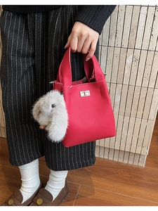 Detail of rose red lychee grain leather bucket bag with silver clasp and plush rabbit charm