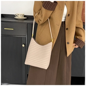 Detail einer minimalistischen cremefarbenen Schultertasche mit gewebtem Design in Halbmondform