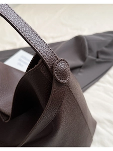 Detail of dark brown lychee leather texture and circular strap fastener on bucket bag