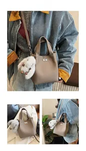 Detail of a brown leather bucket bag featuring a silver twist lock and a plush rabbit charm