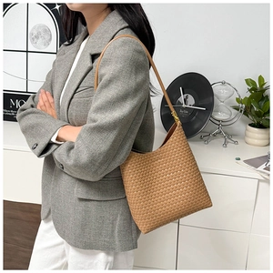 Braune Hobo-Tasche aus geflochtenem Leder, getragen von einem Modell über einem grauen Blazer