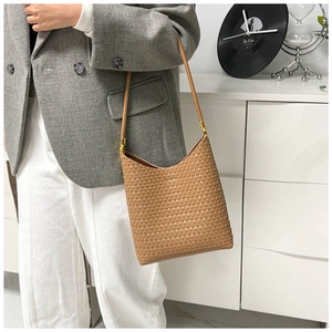 Detail of brown woven tote bag featuring fine leather straps and gold metal hardware