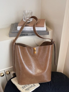 Retro brown leather bucket bag with brass twist lock and wide shoulder strap in soft light
