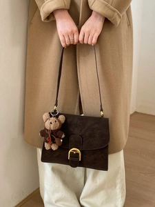 Dark brown suede crossbody bag with gold buckle and plush bear charm on model