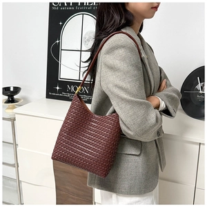 Detail einer dunkelbraunen geflochtenen Ledertasche mit goldener Schnalle an einem Model
