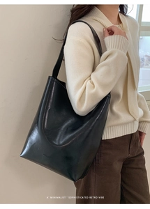 Close-up of minimalist black leather bucket bag with wide shoulder strap on a model