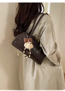 Detail of dark brown vintage leather shoulder bag with plush bear charm and bow