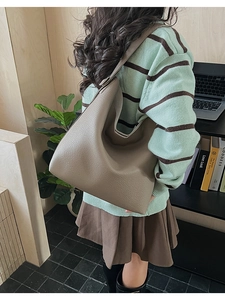 Detailed view of taupe lychee leather tote bag with wide shoulder strap on a model