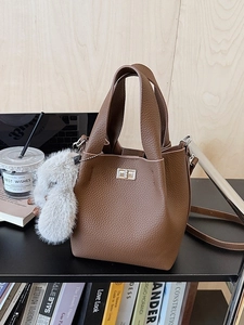 Brown litchi leather bucket bag with silver lock and plush bunny charm on a stand