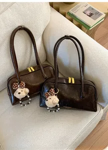 Detail of dark brown leather Boston bag featuring a plush puppy charm and golden zippers