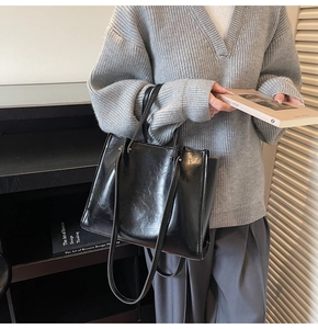 Fashionable black faux leather tote bag with glossy finish held by a model in casual wear