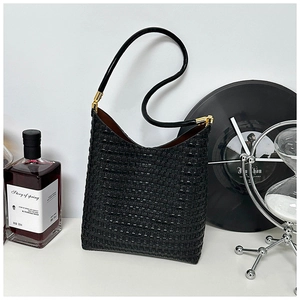 Detail view of black woven tote bag with gold hardware and lifestyle props on white table