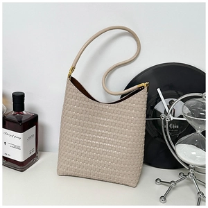 Beige woven texture tote bag with leather handles shown in a minimalist home setting