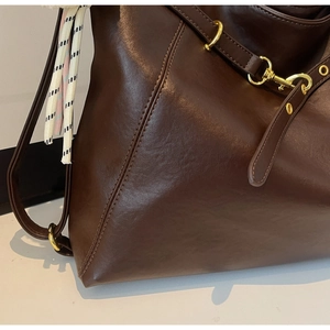 Detail of dark brown leather tote showing gold metal hook and fine stitching craftsmanship
