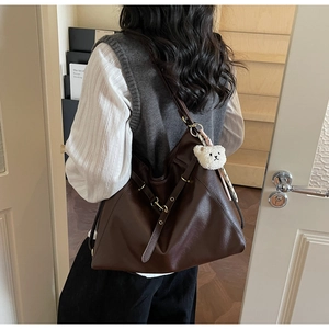 Detail of dark brown leather tote bag with plush bear charm worn by a person