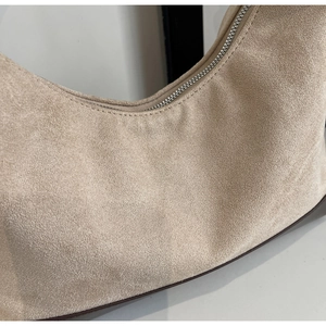 Macro view of beige suede hobo bag with silver metal zipper and brown edge finish