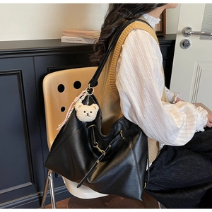 Detailed view of black faux leather tote with golden hardware and white plush bear charm