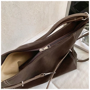 Detailed view of dark brown suede tote bag with white stitching and silver zipper