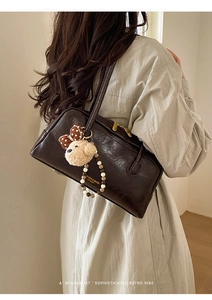 Detail of dark brown leather Boston bag with a cute teddy bear charm and pearl strap