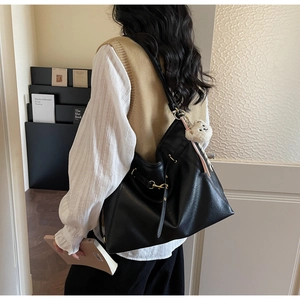 Detail of black tote bag with textured leather, gold buckle, and plush bear charm