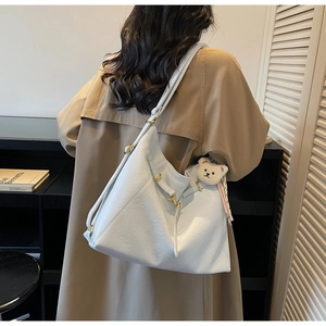 Detail view of large light blue tote bag on shoulder with white bear plush charm