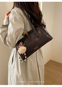 Detail of dark brown vintage shoulder bag with plush bear charm on beige trench coat