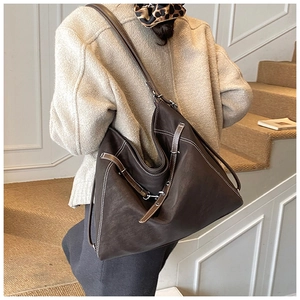 Detail of dark brown leather tote bag showing white contrast stitching and metal side buckle