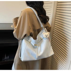 Detail of light blue faux leather tote bag with gold buckle and plush bear charm