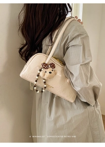 Detail of cream pleated leather bag with gold hardware and plush bear charm decoration