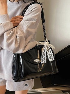 Black patent leather tote bag with silver twist lock and lace bow charm on a model
