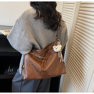Detailed back view of a large brown tote bag with leather straps and bear charm