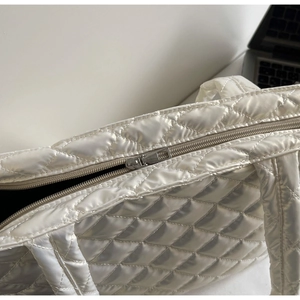 Detail of white quilted tote bag featuring smooth zipper closure and neat diamond stitching