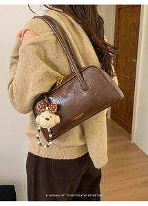 Detail of dark brown retro leather underarm bag with cute plush bear charm and gold zippers