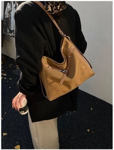 Outdoor shot of a tan faux leather tote bag with white contrast stitching and slim straps