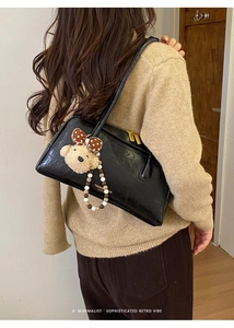 Detailed side view of vintage black leather Boston bag with teddy bear charm on model